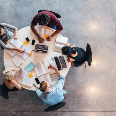 an aerial view of five people sitting at a table with laptops and open books